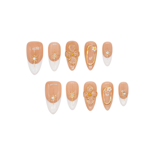Medium almond press-on nails in nude and white French tips with 3D gold flowers, gemstone accents, and gold frames.