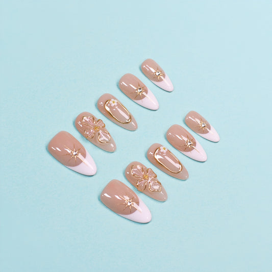 Medium almond press-on nails in nude and white French tips with 3D gold flowers, gemstone accents, and gold frames.