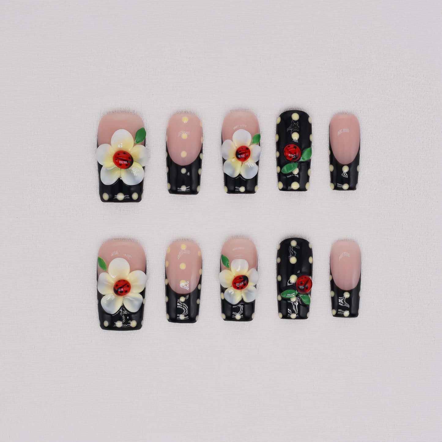 Handmade black French tip press-on nails with floral art, polka dot details, and 3D ladybug accents in glossy salon-quality finish