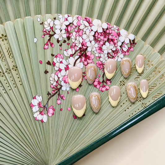 Citrine Silk Veil nude press-on nails with pale yellow French tips and sculpted gold frames — styled product photograph.