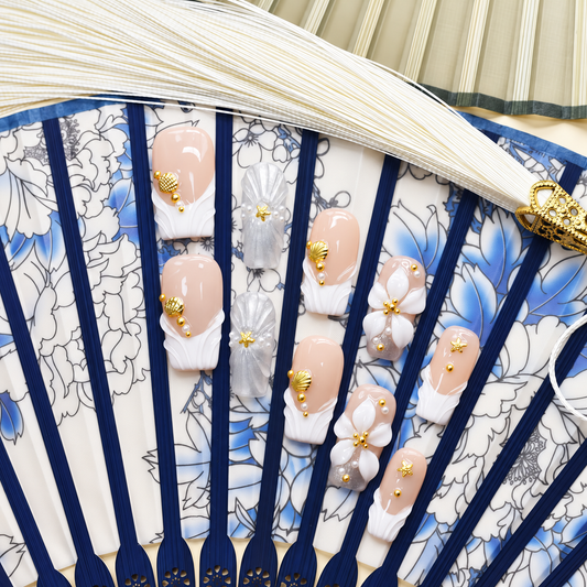 Golden Shell Garden nude press-on nails with gold shells, starfish, pearls and white flowers — styled product photograph.