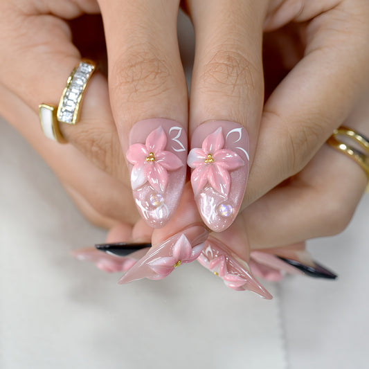 Luxury pink floral press-on nails with 3D flower design, pearl embellishments, and black French tip accents displayed on beige textured background