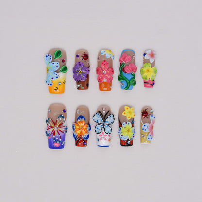 Handmade colorful floral press-on nails with 3D flower art, butterfly-inspired details, rhinestones, and glossy artistic finish