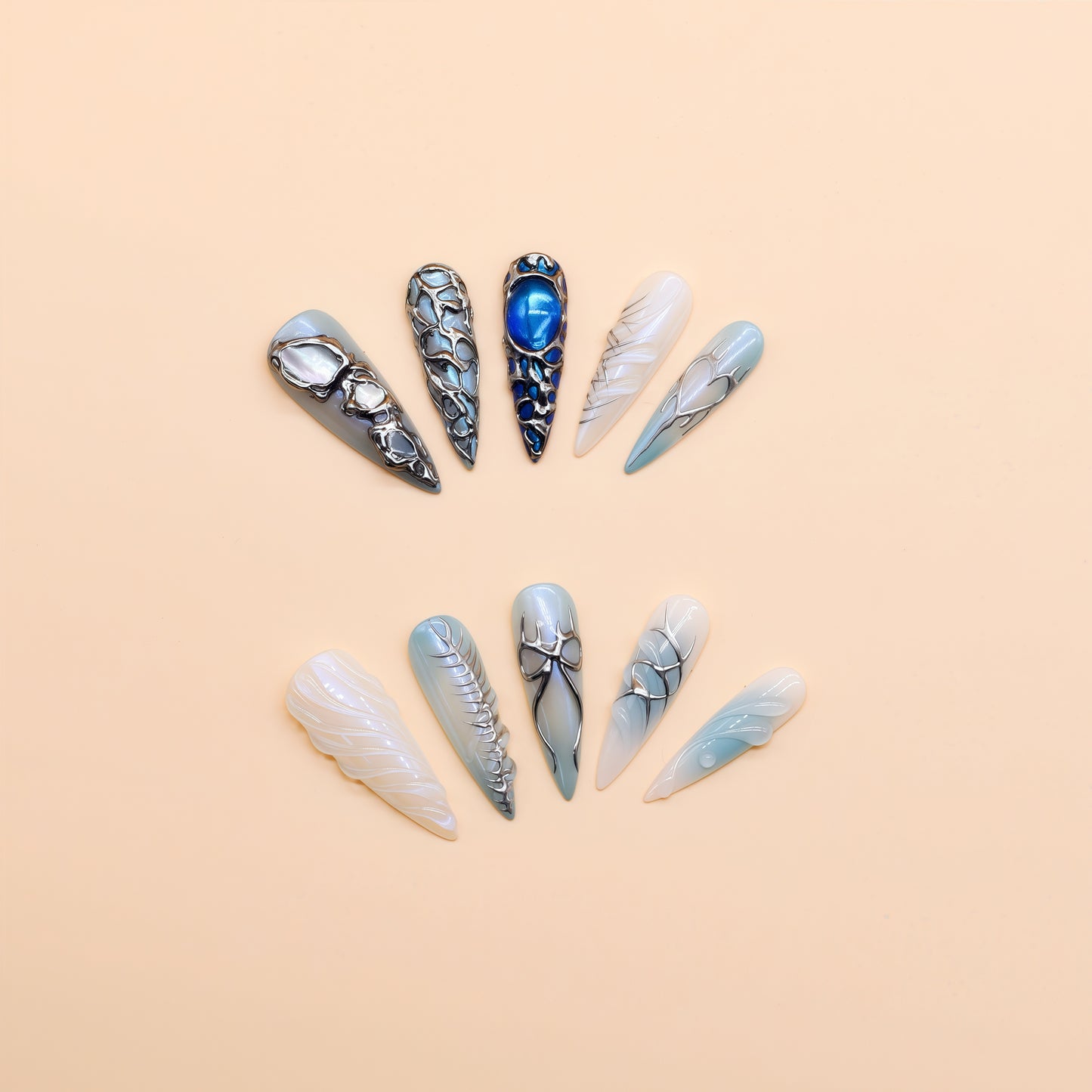 Long stiletto press-on nails in icy blue and silver with chrome textures, gemstone accents, and futuristic 3D design.
