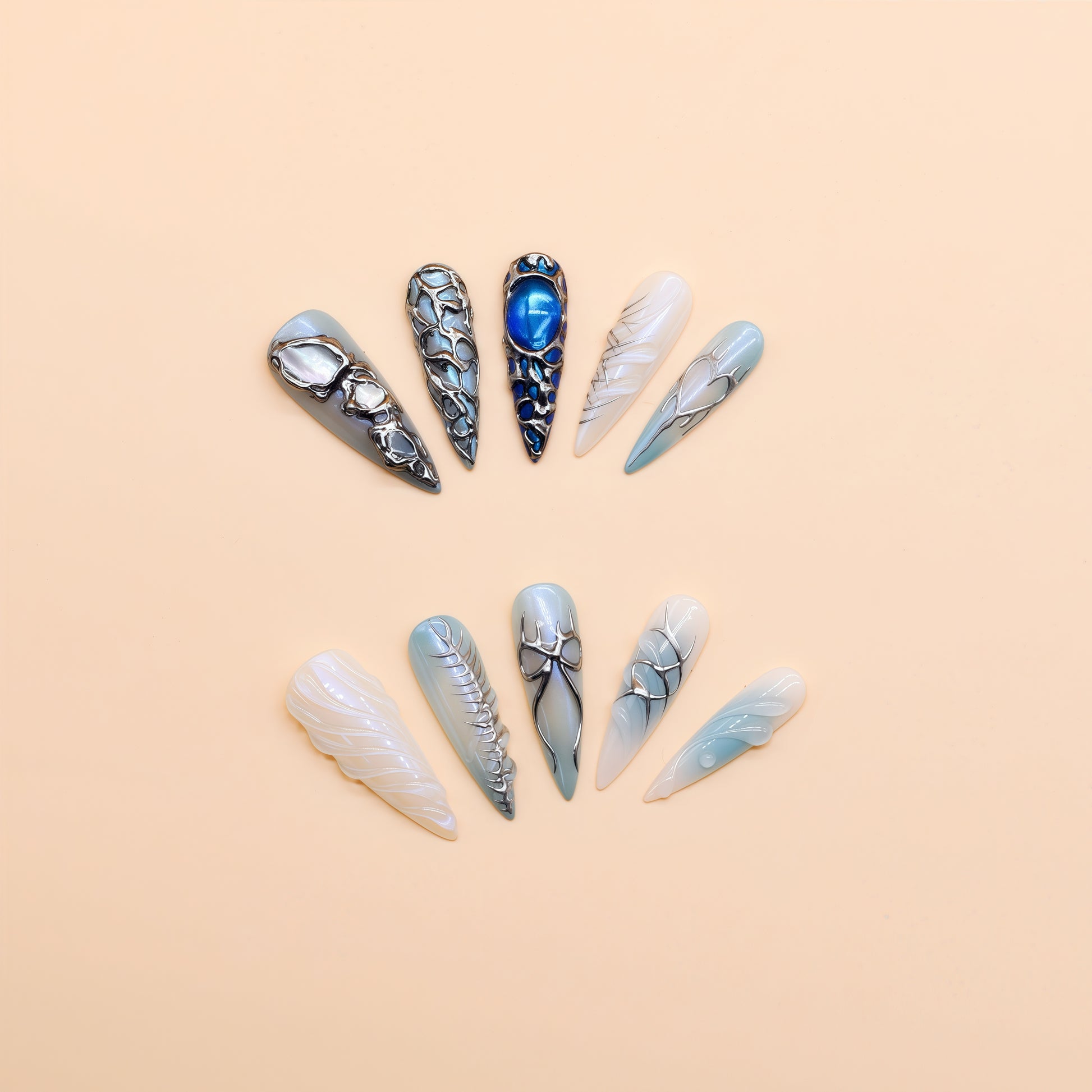 Long stiletto press-on nails in icy blue and silver with chrome textures, gemstone accents, and futuristic 3D design.