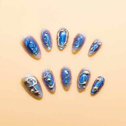 Almond-shaped press-on nails in holographic blue with silver chrome lines and 3D metallic accents – Blue Steel Siren set.