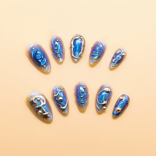 Almond-shaped press-on nails in holographic blue with silver chrome lines and 3D metallic accents – Blue Steel Siren set.