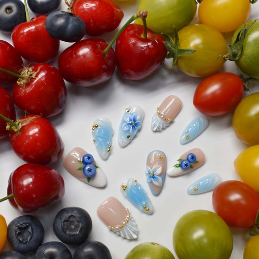 Pastel blue and nude press on nails with blueberry artwork, seashell accents and floral details.