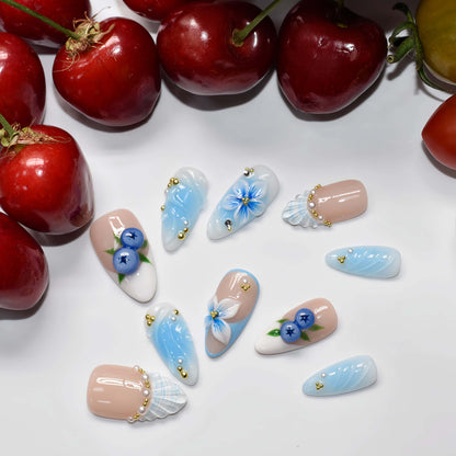 Pastel blue and nude press on nails with blueberry artwork, seashell accents and floral details.