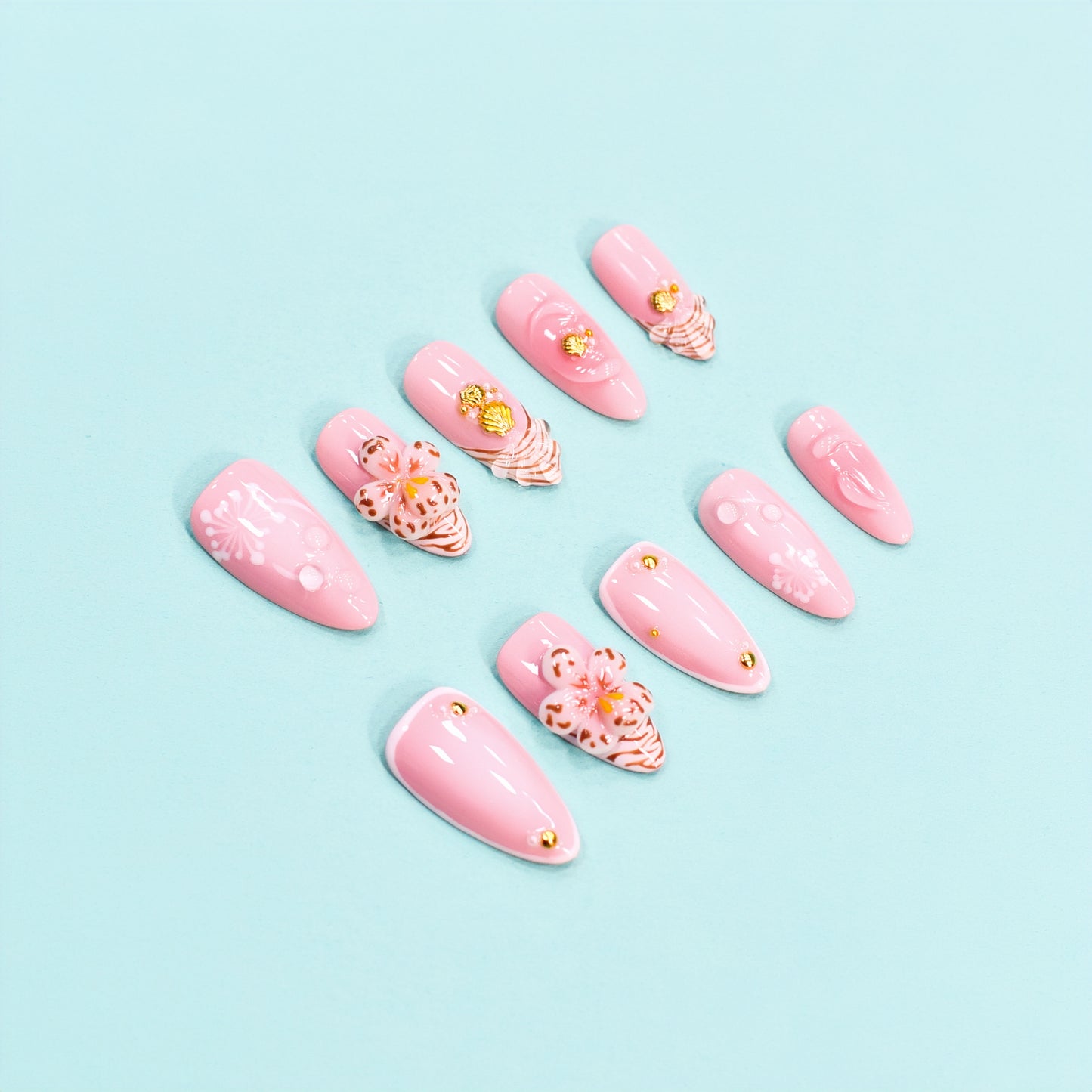 Medium almond press-on nails in soft pink with 3D floral appliqués, white botanical detailing, and gold seashell accents – Blush Bloom nail set.
