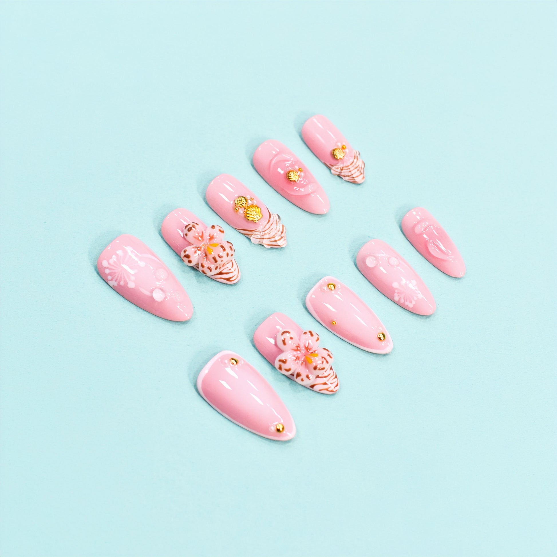 Medium almond press-on nails in soft pink with 3D floral appliqués, white botanical detailing, and gold seashell accents – Blush Bloom nail set.