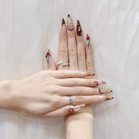 Long stiletto press-on nails in deep red gradient with 3D cherries, gold flowers, and floral hand-painted designs – Cherry Ember by You Are Angel.