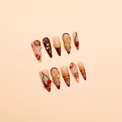 Long stiletto press-on nails in deep red gradient with 3D cherries, gold flowers, and floral hand-painted designs – Cherry Ember by You Are Angel.
