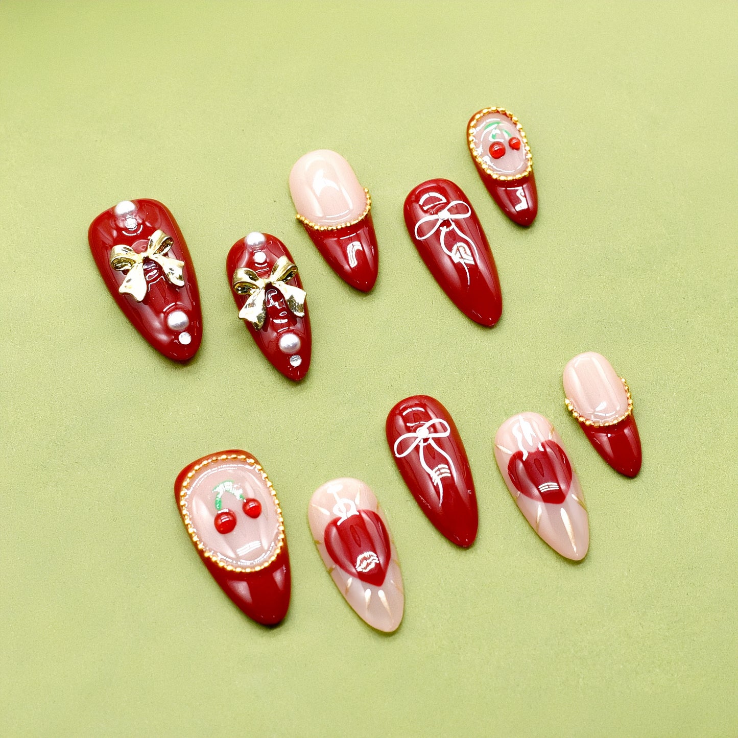Cherry Kiss & Crimson Bows press-on nails with red and nude tones, 3D cherry and gold bow charms, heart and ribbon accents, almond shape.
