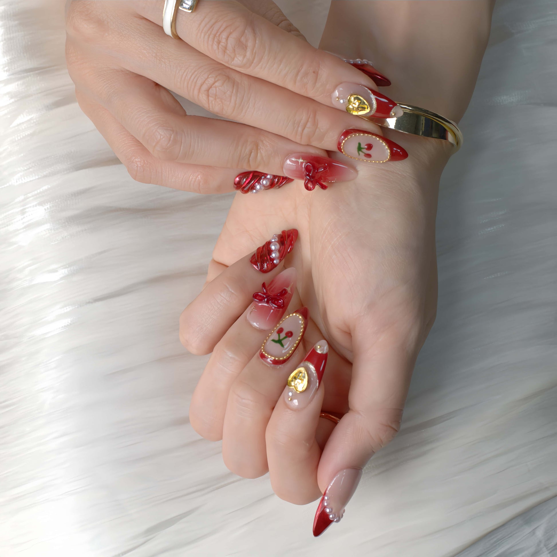 Cherry Luxe Charm press-on nails in red chrome and nude tones with pearl trims, gold accents, and cherry details — festive and elegant.