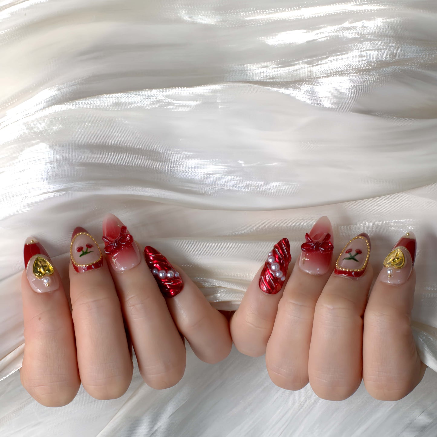 Cherry Luxe Charm press-on nails in red chrome and nude tones with pearl trims, gold accents, and cherry details — festive and elegant.