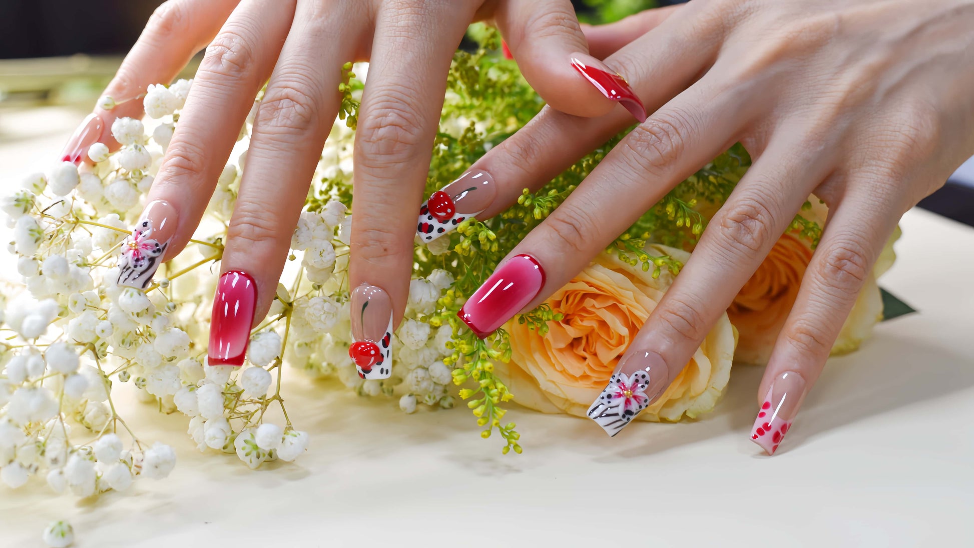 Handmade cherry-red floral press-on nails with glossy ombré finish, cherry accents, and elegant black-and-white artistic nail art
