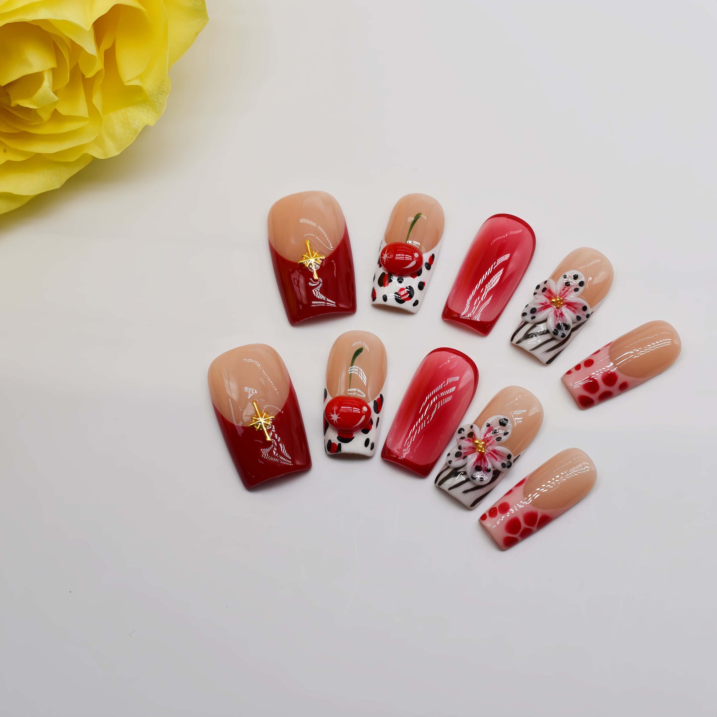 Handmade cherry-red floral press-on nails with glossy ombré finish, cherry accents, and elegant black-and-white artistic nail art