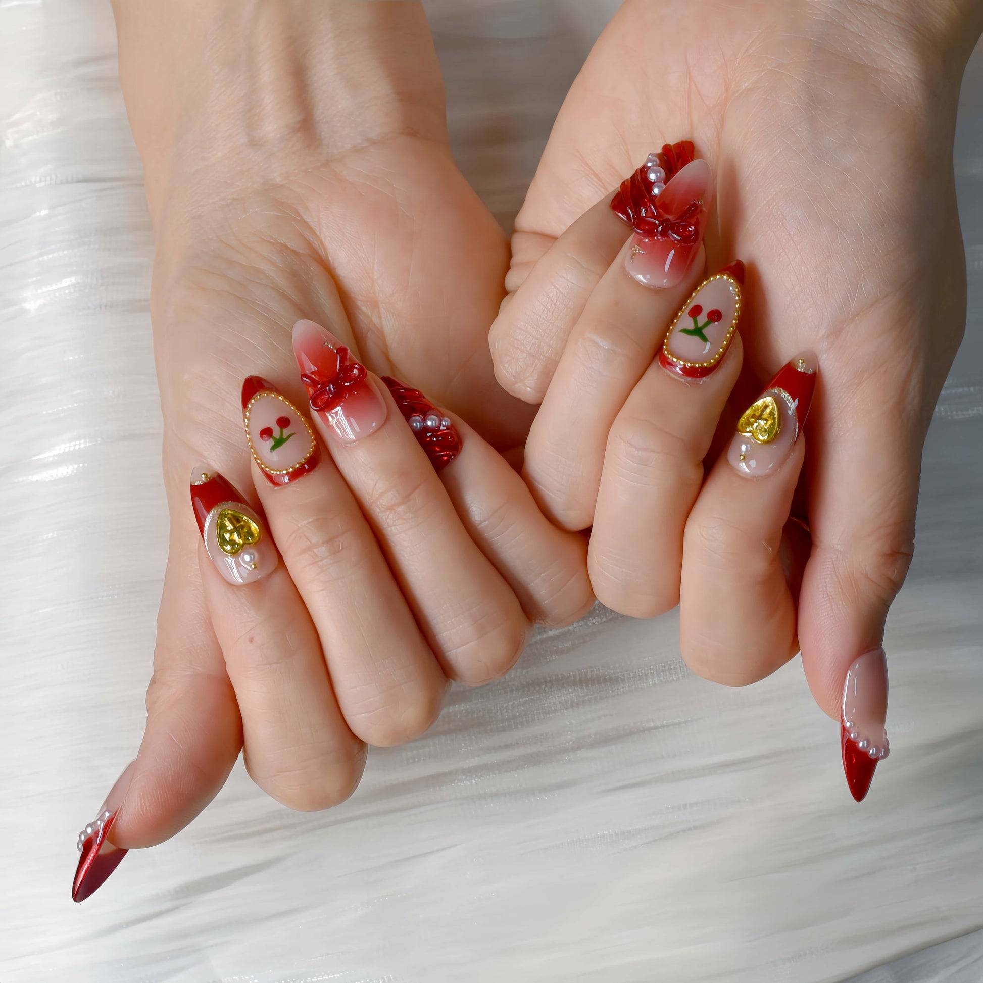 Cherry Luxe Charm press-on nails in red chrome and nude tones with pearl trims, gold accents, and cherry details — festive and elegant.