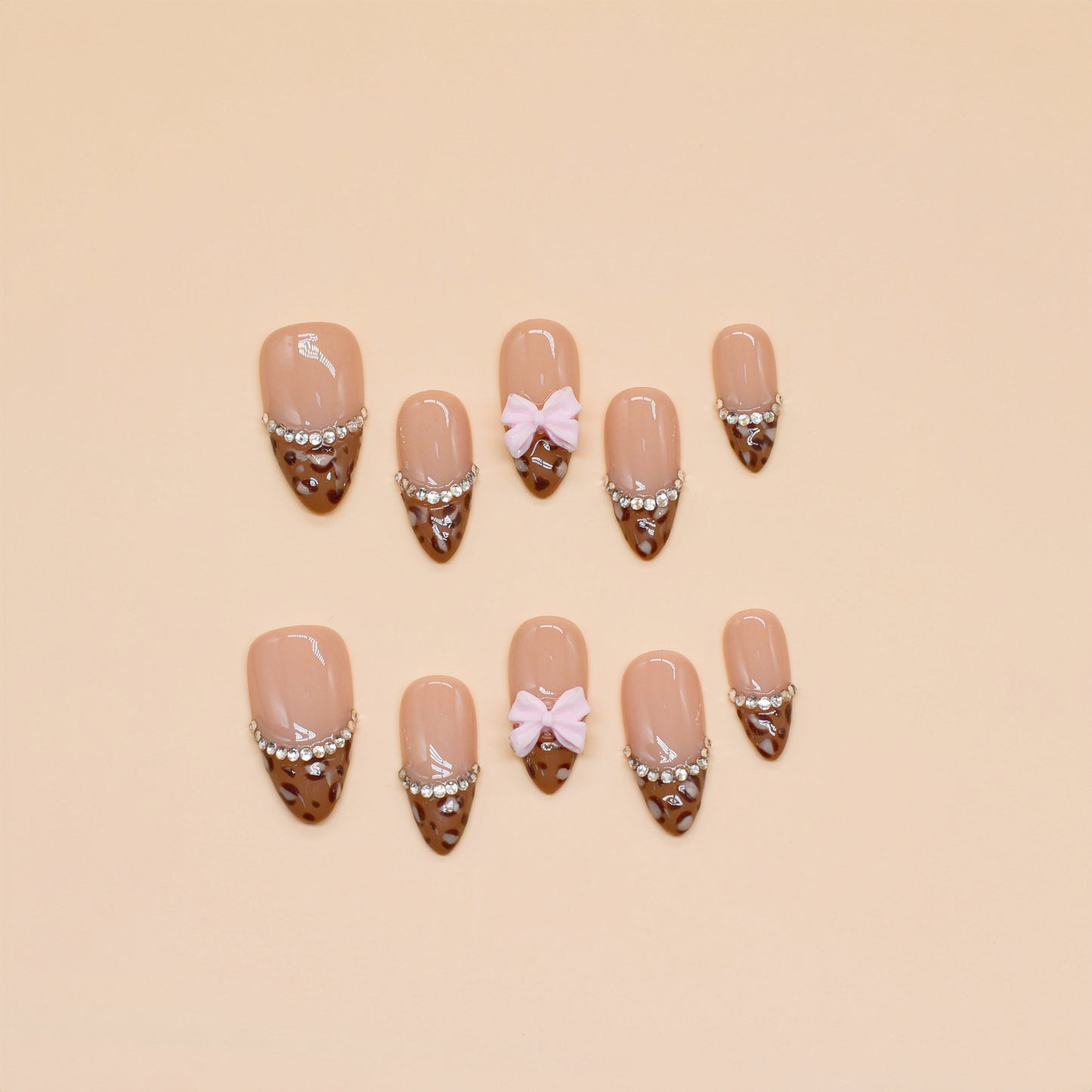 Choco Chic press-on nails by You Are Angel with brown tips, silver gem chains, nude base, and pink 3D bows.