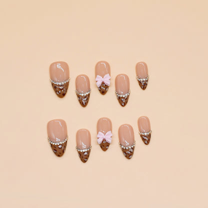 Choco Chic press-on nails by You Are Angel with brown tips, silver gem chains, nude base, and pink 3D bows.