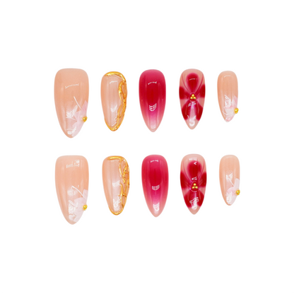 Medium almond press-on nails in nude and crimson ombré with white florals, gold beads, and sculpted gold frame.