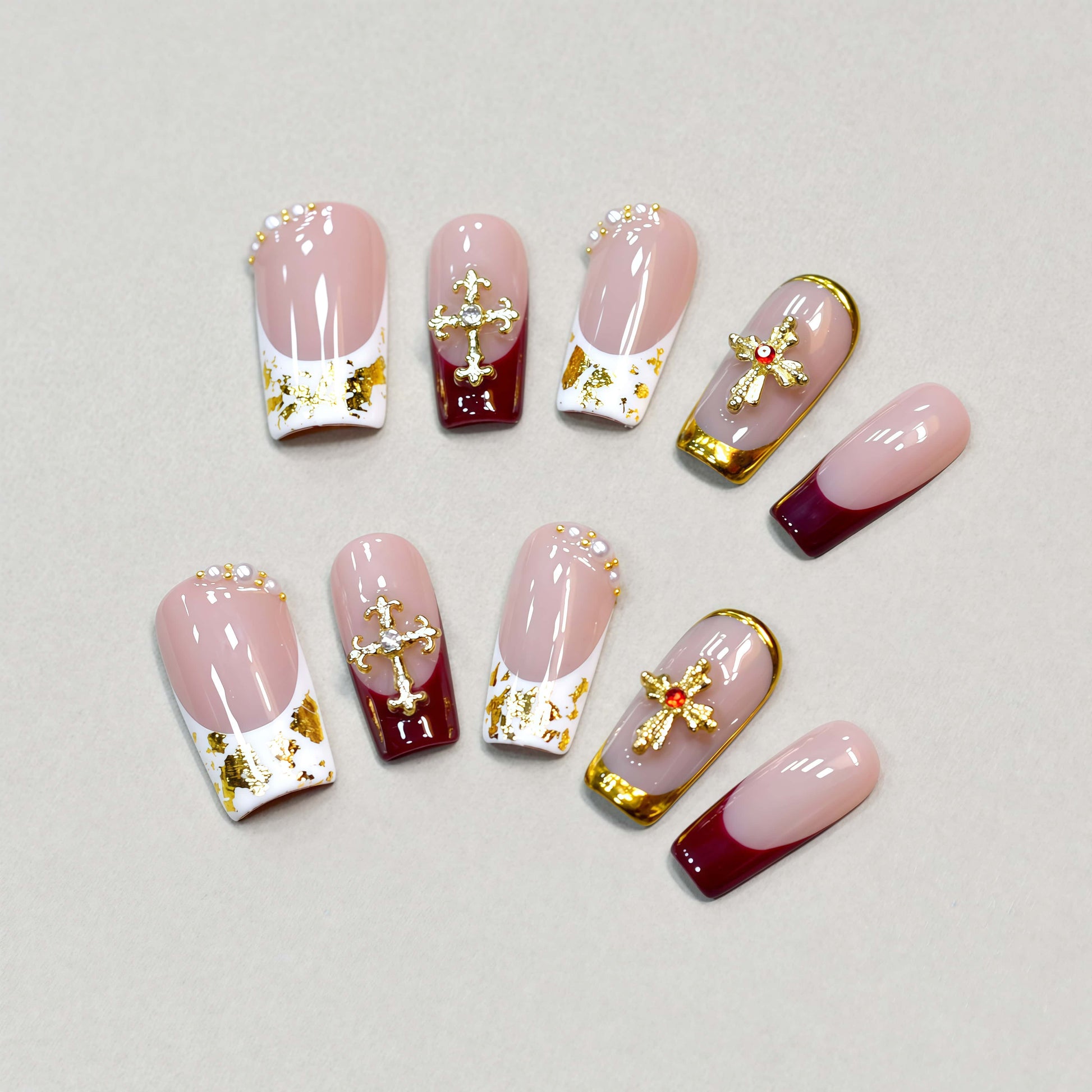 Crimson Grace press-on nails featuring red and nude tones, gold crosses, pearls, and metallic gold frames for a luxurious festive look.