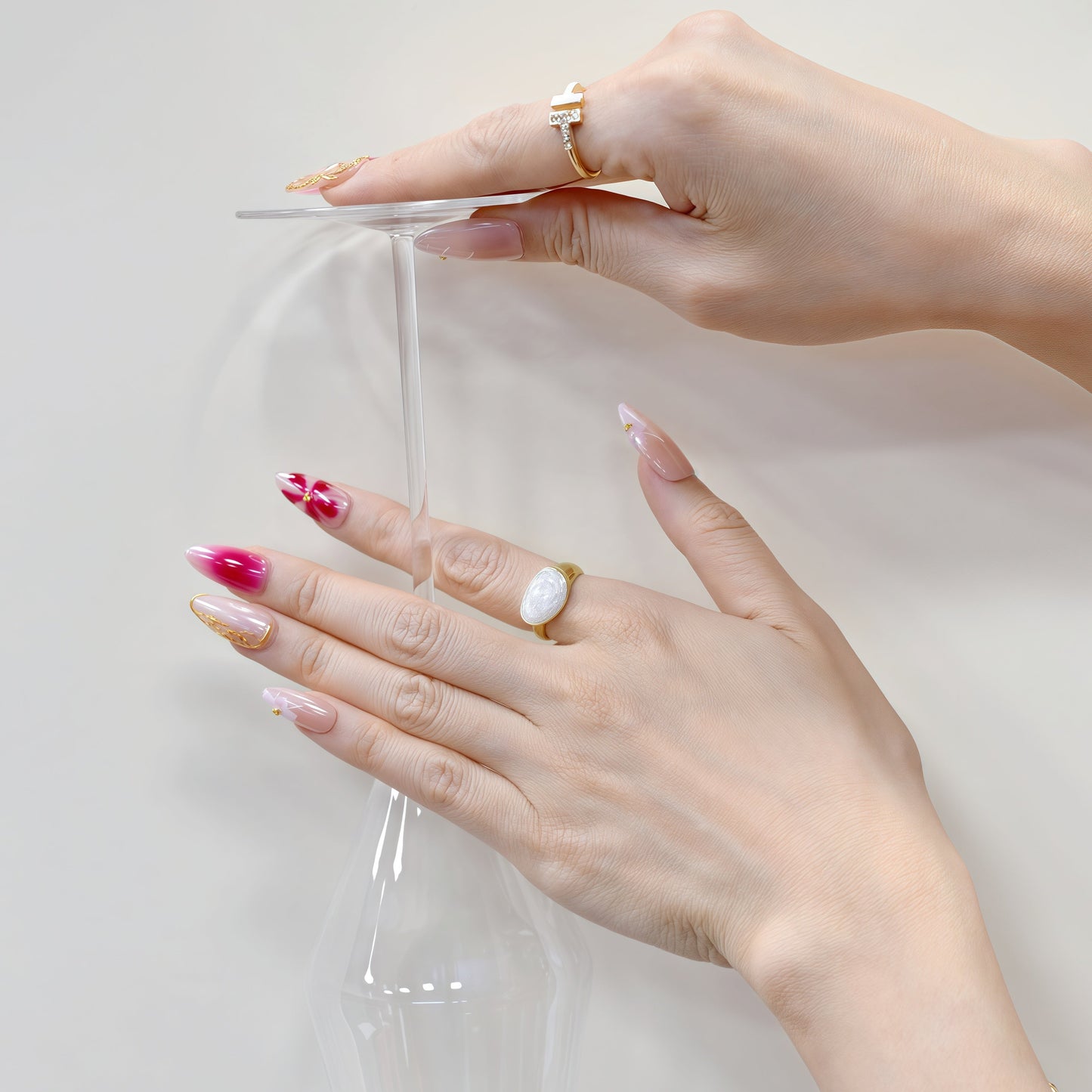 Medium almond press-on nails in nude and crimson ombré with white florals, gold beads, and sculpted gold frame.