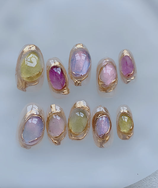 Handmade press-on nails with pastel jelly tones and gold-framed detailing, inspired by stained glass and soft blooming colors.