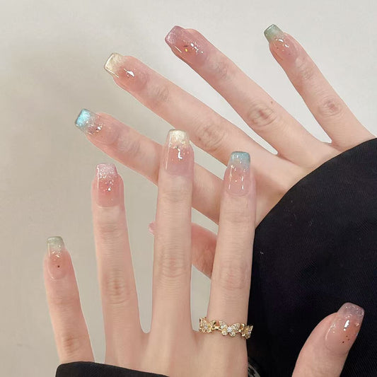 Hand wearing Éclat Nailery’s Champagne Cloud press-on nails – nude base with champagne glitter ombré, square shape, elegant and minimalist design.