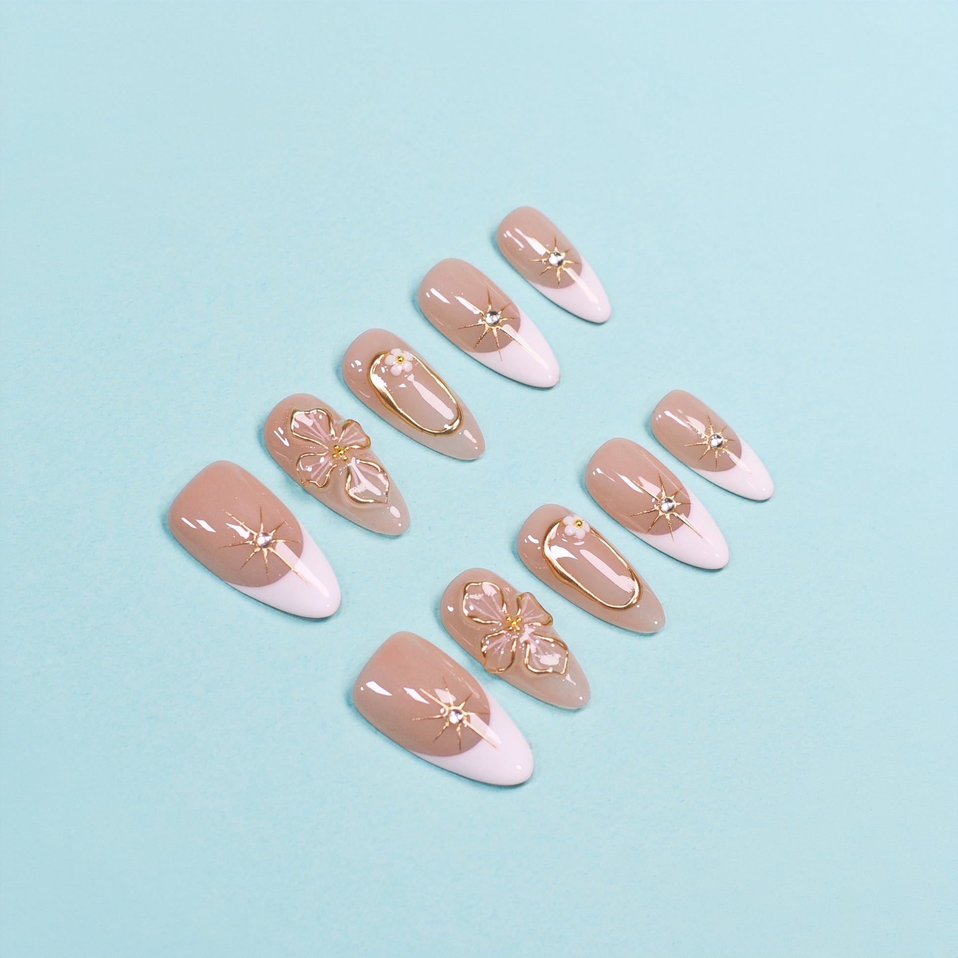 Medium almond press-on nails in nude and white French tips with 3D gold flowers, gemstone accents, and gold frames.