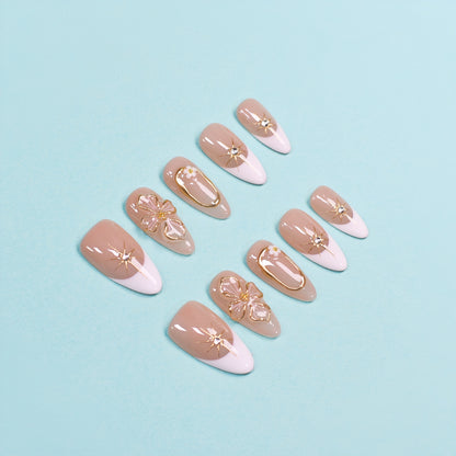 Medium almond press-on nails in nude and white French tips with 3D gold flowers, gemstone accents, and gold frames.
