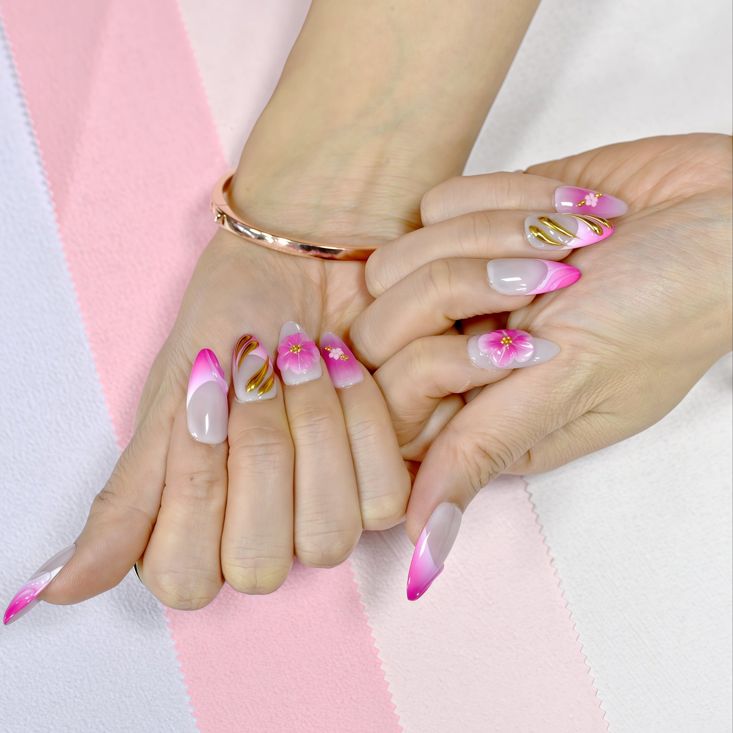 Medium almond press-on nails in pink ombré with 3D pink flowers, gold sculpting, and floral accents.
