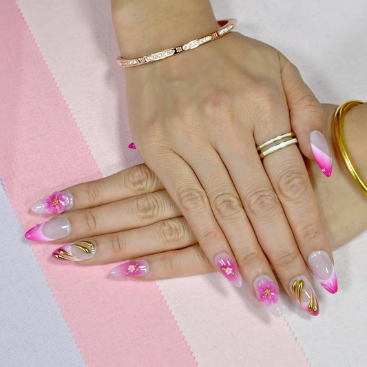 Medium almond press-on nails in pink ombré with 3D pink flowers, gold sculpting, and floral accents.