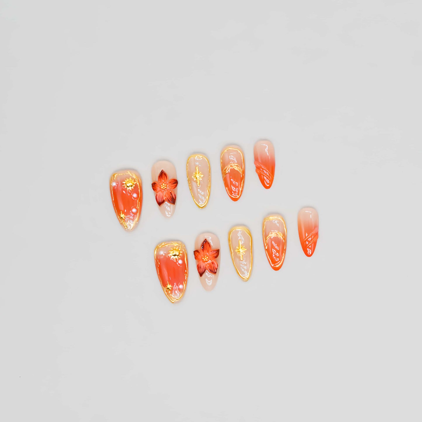 Golden Ember Bloom press-on nails in amber-orange with gold contour lines and red floral 3D accents, captured under blue sky lighting.