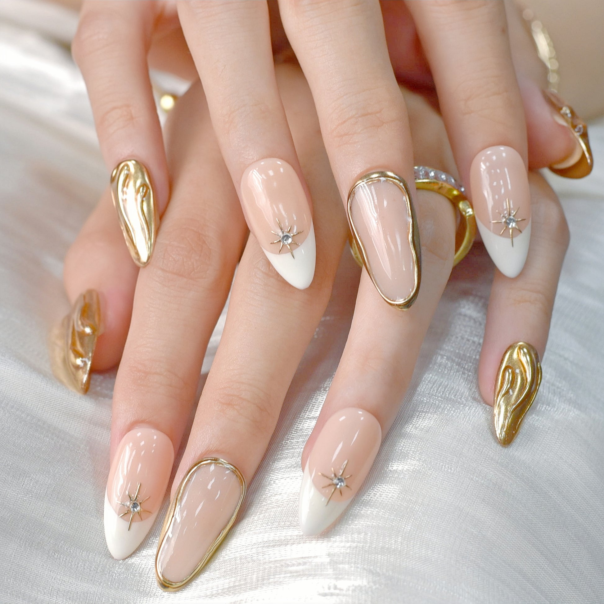 Luxury nude and white French tip press-on nails with gold chrome accents and star gem details displayed on a soft white background