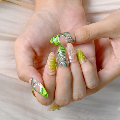 Close-up of hands with green and clear leaf-themed nail art on a light background