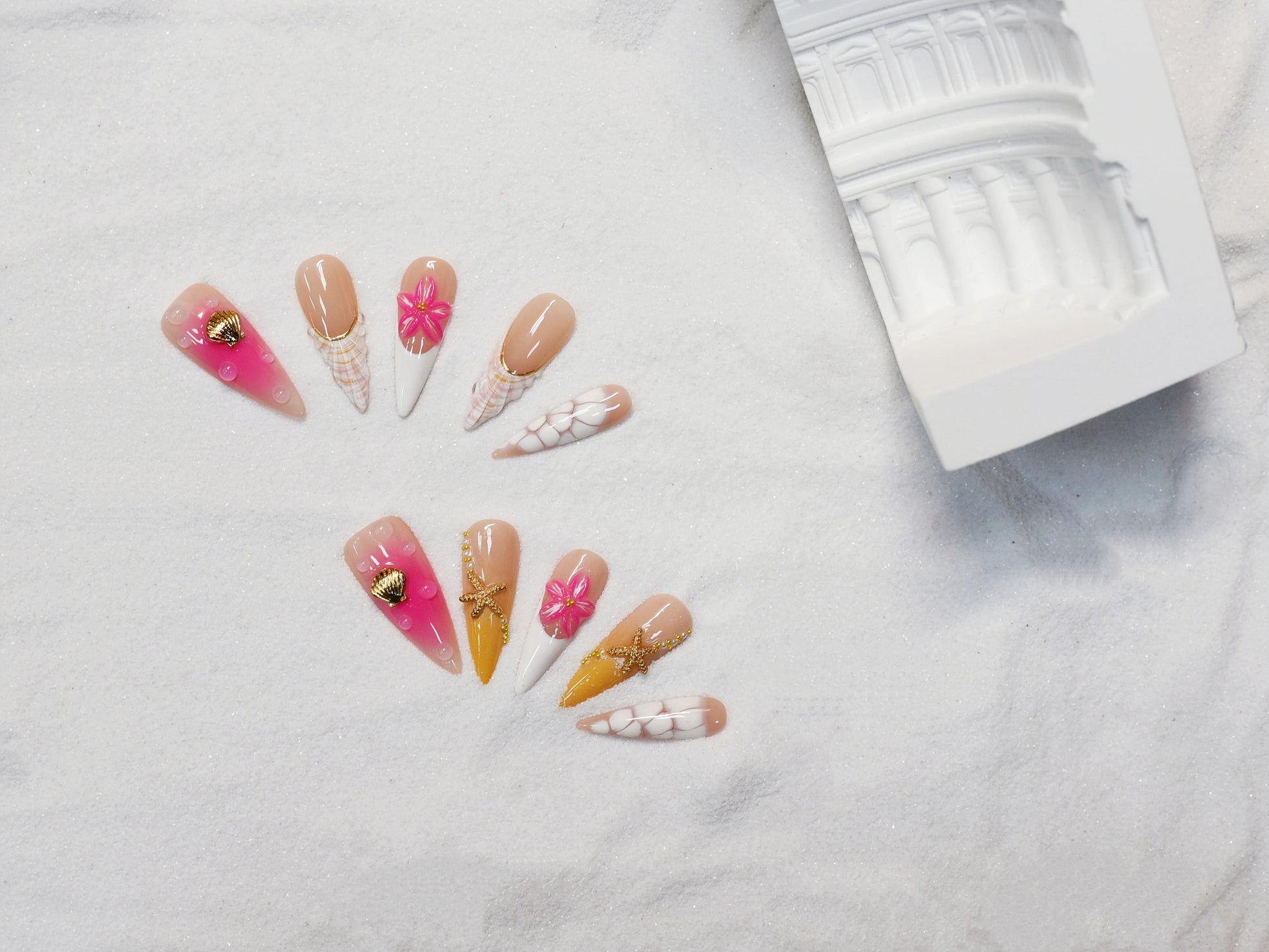 Long stiletto tropical press-on nails featuring vibrant pink and orange gradients, 3D starfish and gold seashell accents – Island Glow nail set.