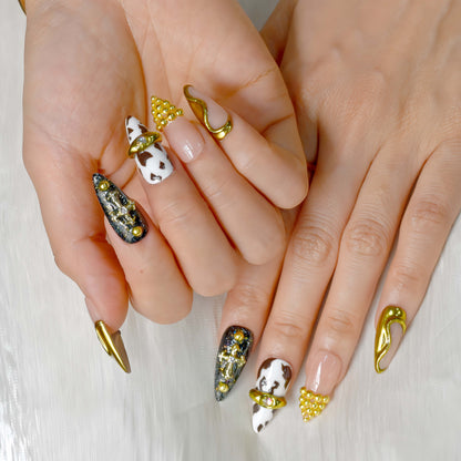Midnight Rodeo press-on nails featuring gold metal accents, black glitter, cow print, and nude tones for a bold Western-glam look.