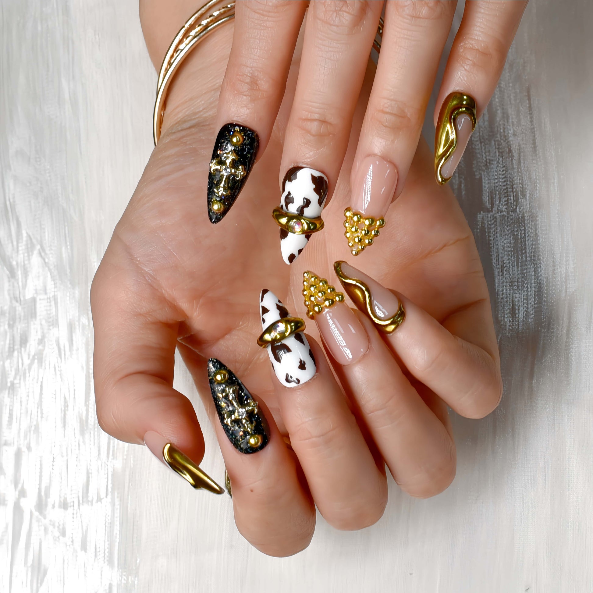 Midnight Rodeo press-on nails featuring gold metal accents, black glitter, cow print, and nude tones for a bold Western-glam look.