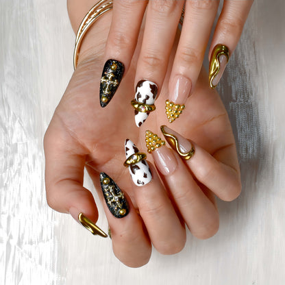 Midnight Rodeo press-on nails featuring gold metal accents, black glitter, cow print, and nude tones for a bold Western-glam look.