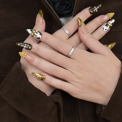 Midnight Rodeo press-on nails featuring gold metal accents, black glitter, cow print, and nude tones for a bold Western-glam look.