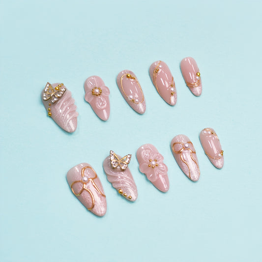 Peach-toned press-on nails with rhinestone butterfly, gold bow details, and 3D floral accents – by You Are Angel.