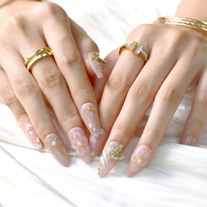 Peach-toned press-on nails with rhinestone butterfly, gold bow details, and 3D floral accents – by You Are Angel.