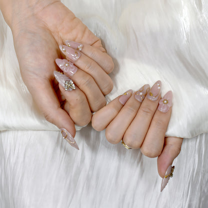 Peach-toned press-on nails with rhinestone butterfly, gold bow details, and 3D floral accents – by You Are Angel.