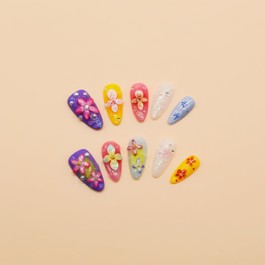 Medium almond press-on nails with bright floral 3D designs in purple, pink, yellow, and white – Petal Parade handmade nail set.