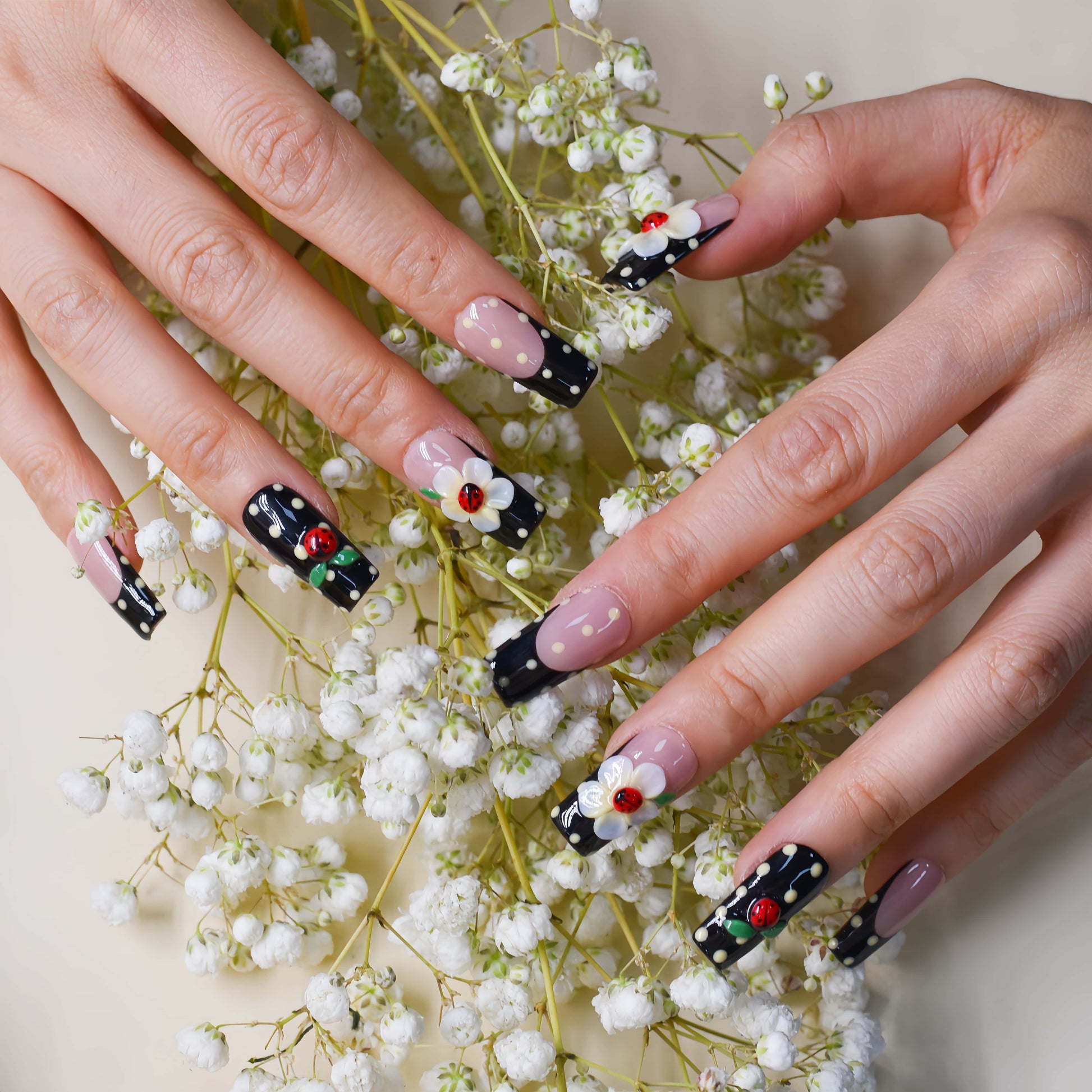 Handmade black French tip press-on nails with floral art, polka dot details, and 3D ladybug accents in glossy salon-quality finish