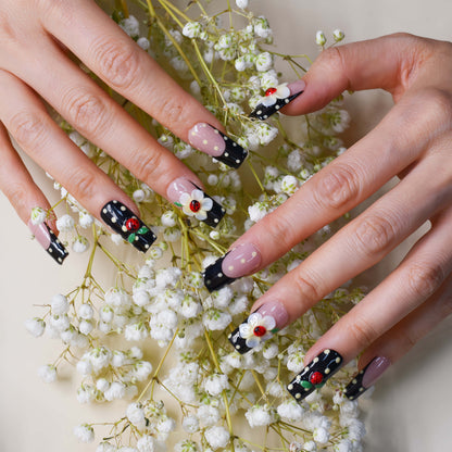 Handmade black French tip press-on nails with floral art, polka dot details, and 3D ladybug accents in glossy salon-quality finish