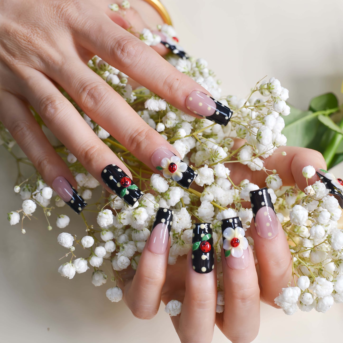 Handmade black French tip press-on nails with floral art, polka dot details, and 3D ladybug accents in glossy salon-quality finish