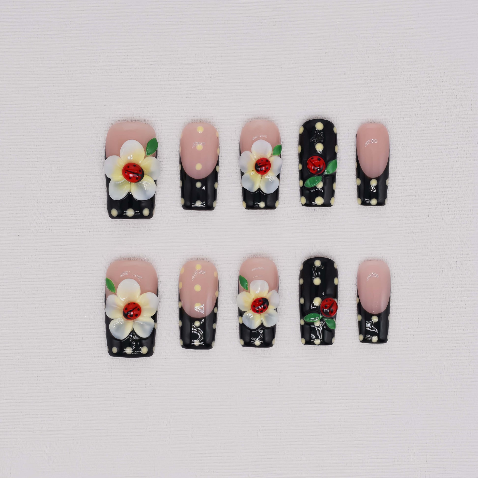 Handmade black French tip press-on nails with floral art, polka dot details, and 3D ladybug accents in glossy salon-quality finish